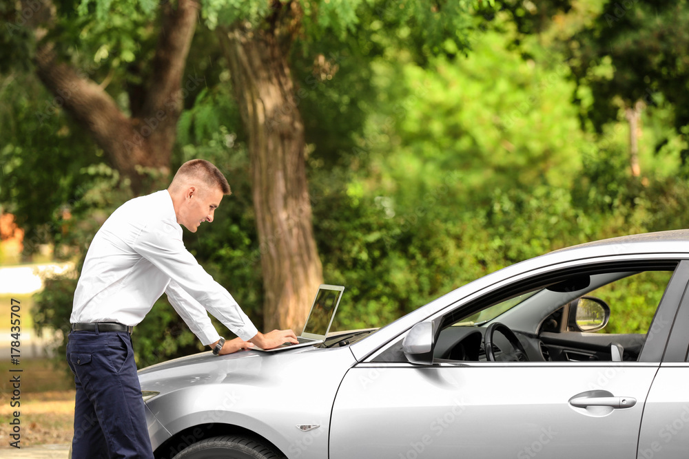 Handsome young businessman using laptop near car in park Handsome young businessman using laptop near car in park