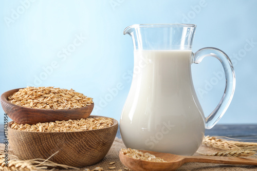Wooden bowls with oatmeal flakes and pitcher of milk on light background