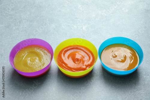 Bowls with baby food on grey background