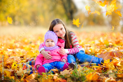 girl hugging younger sister sitting on fall fallen foliage.