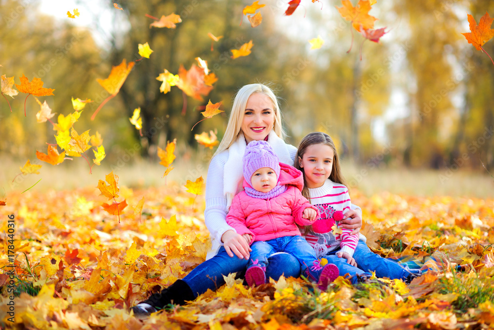 happy family, mum sits with children on the grass under falling autumn leaves. happy family, mum sits with children on the grass under falling autumn leaves.