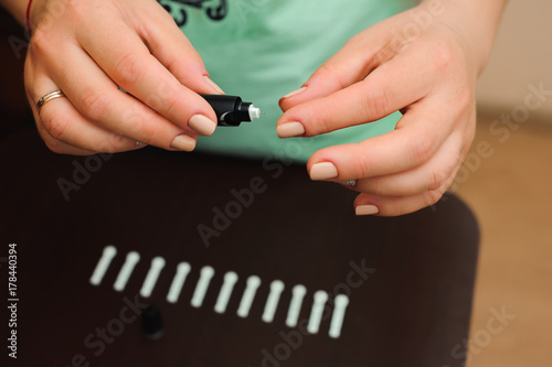 Woman taking blood sample with lancet pen on wooden background. Diabetes concept.