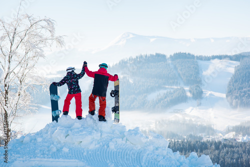 Couple snowboarders high fiving each other, standing on top of a snowy mountain, observing stunning winter view, resting after snowboarding at ski resort on a beautiful sunny winter day, Bukovel