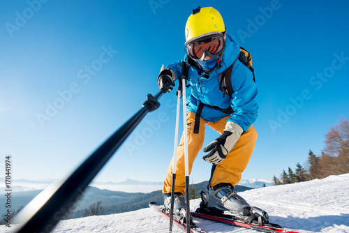 Low angle shot of a professional skier taking a selfie using monopod posing on top of a slope in the mountains, copyspace ski resort recreation travelling tourism vacation extreme adrenaline