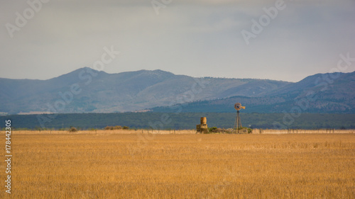 Fallow wheat field with a water pump windmill with mountains in the background.  South Africa