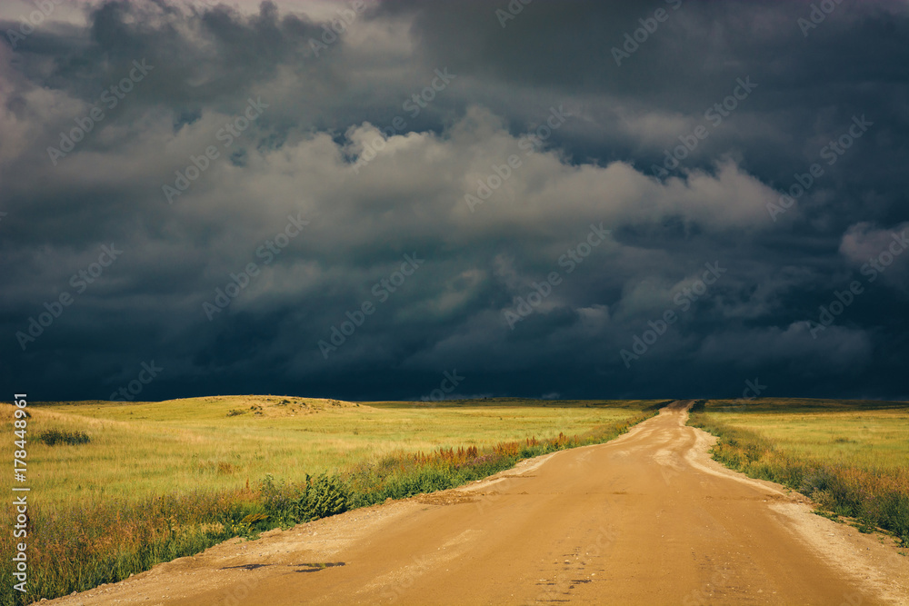 Dramatic dark storm clouds and dirt road to the horizon line. Dramatic dark storm clouds and dirt road to the horizon line.