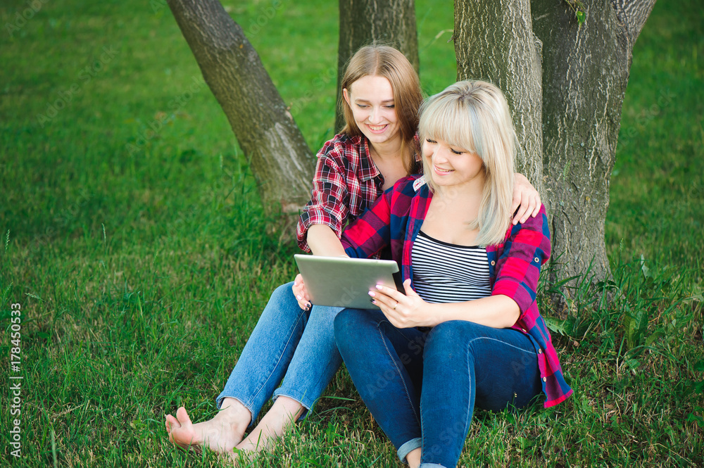 Smiling women using tablet ps on a green meadow Smiling women using tablet ps on a green meadow