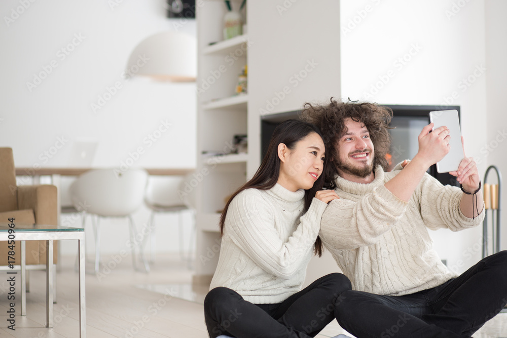 multiethnic couple using tablet computer in front of fireplace multiethnic couple using tablet computer in front of fireplace