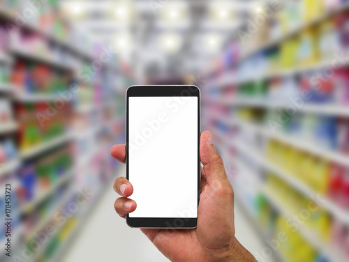 Man's hand holding blank white screen mobile phone on blurred supermarket background