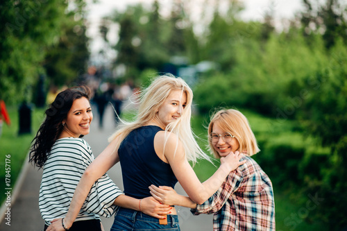 Back view of three beautiful women sitting on grass and hugs photo