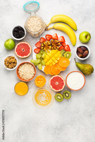 Fototapeta Naklejka Na Ścianę i Meble -  Above view of healthy breakfast with oats, variety of fruits, strawberries, mango, grapes, served on the white table, selective focus