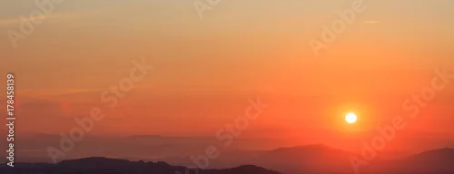 Obraz  z motywem Beautiful sunset on sky over mountains background. The sun is on the right side.