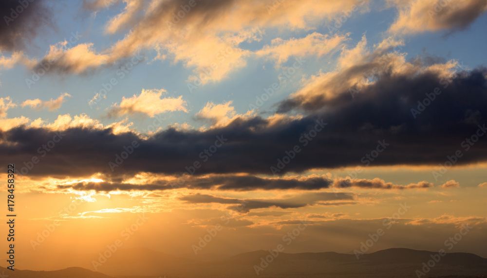 Beautiful sunset on sky. Gold sun lightens the clouds over mountains. The sun is on the left side.