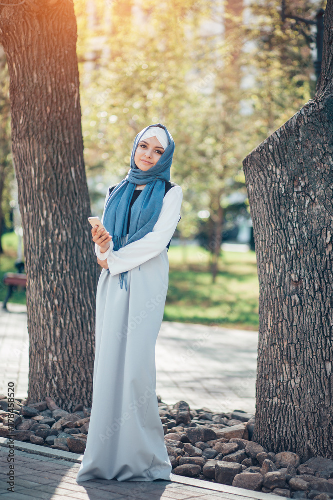 Beautiful muslim girl in blue hijab looking in camera. Full length 