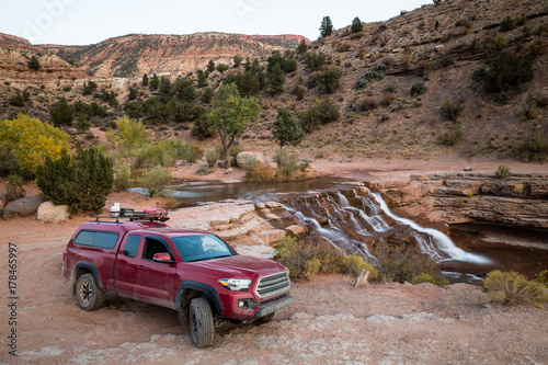 Red pickup camping rig on rocky trail near waterfall in southern Utah photo