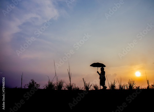 The boy is walking  holding an umbrella on a meadow at sunset.