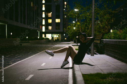 young woman with beautiful feet dressed in white sneakers and black dress, against a backdrop of urban landscapes. Street fashion. night dark style © evgeniykleymenov