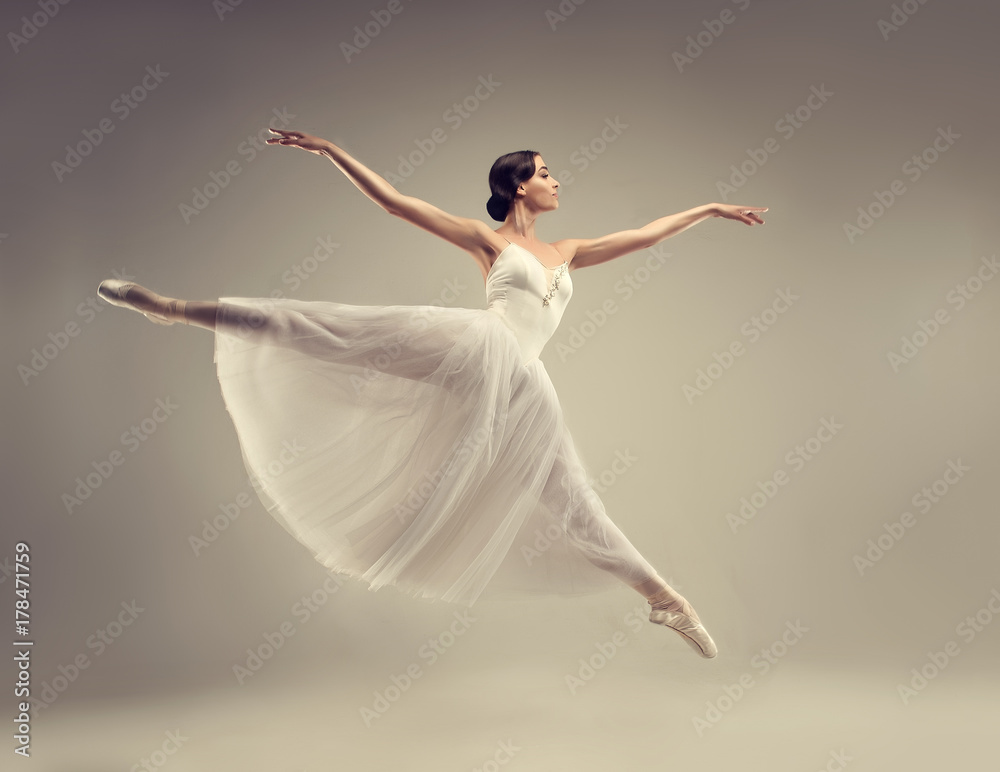 Fototapeta premium Balerina. Młoda tancerka baletowa pełna wdzięku, ubrana w profesjonalny strój, buty i białą nieważką spódnicę demonstruje umiejętności taneczne. Piękno klasycznego baletu.
