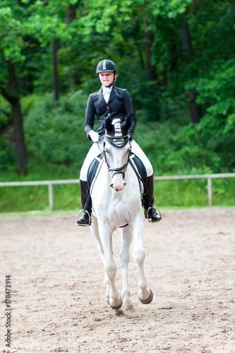 Teenage girl equestrian in dress uniform riding horseback on arena