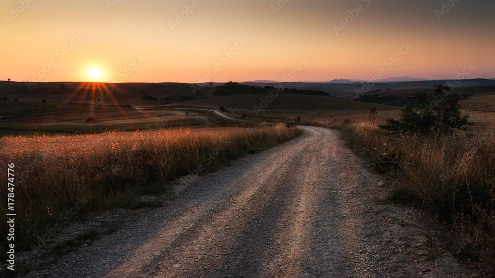 strada sterrata con a fianco campi di grano e cielo al tramonto
