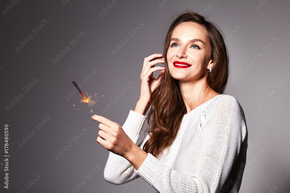Obraz premium Beautiful young sexy brunette long curly hair woman bright makeup red lipstick dressed in knitted white winter sweater holds in hand bengal lights smile holiday new year christmas party fun golden.