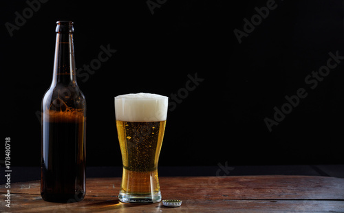 A bottle and a glass of beer on a wooden table, dark background