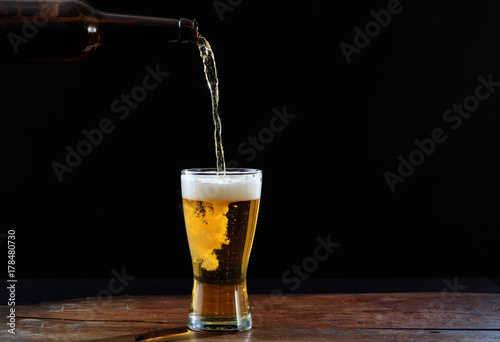 Pouring beer in a glass on a wooden table, dark background