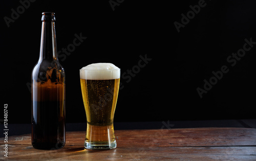 A bottle and a glass of beer on a wooden table, dark background