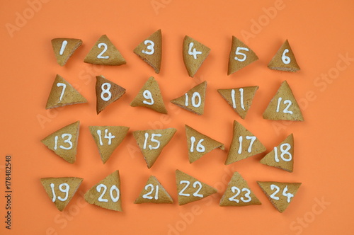 twenty-four numbered and sorted advent cookies on orange background
