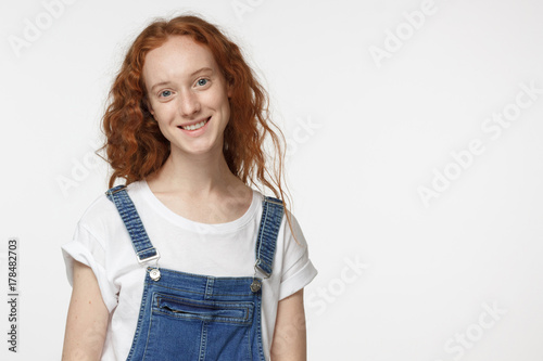 Portrait of smiling attractive curly redhead female isolated on gray background
