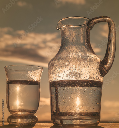 Glass  of  Water and  Pitcher, on blue sky  background,  outdoors, vertical, toning. photo