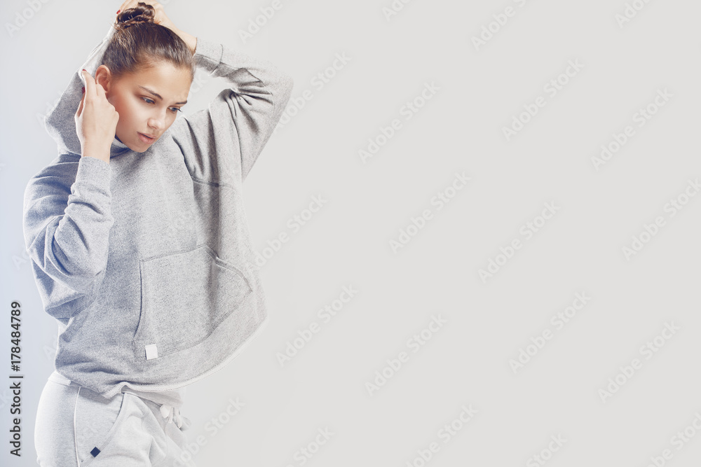 Studio portrait of a young Caucasian girl in a gray sweatshirt. A beautiful girl puts a hood on her head. Gray studio background. Studio portrait of a young Caucasian girl in a gray sweatshirt. A beautiful girl puts a hood on her head. Gray studio background.