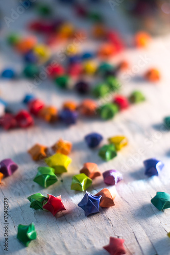 Multicolored paper stars on a wooden white background.