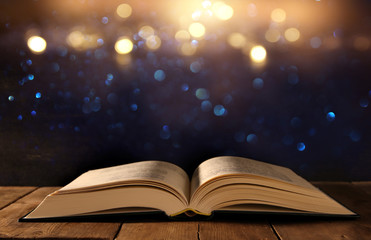 image of open antique book on wooden table with glitter background
