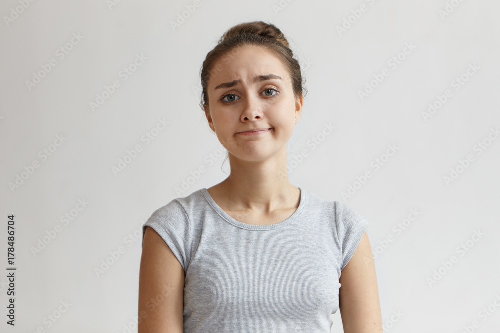Portrait of upset hopeless young female with blue eyes and hair knot frowning eyebrows and looking at camera with disappointed smile, her look expressing sorrow as if she sas: It is what it is Portrait of upset hopeless young female with blue eyes and hair knot frowning eyebrows and looking at camera with disappointed smile, her look expressing sorrow as if she sas: It is what it is