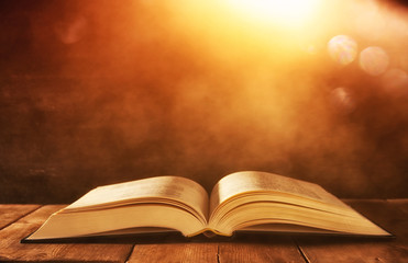 image of open antique book on wooden table with glitter background