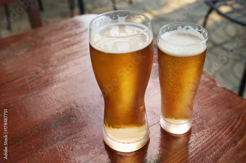 Glasses of fresh beer on wooden table outdoors