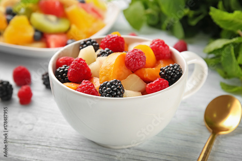 Cup with delicious fruit salad on wooden table