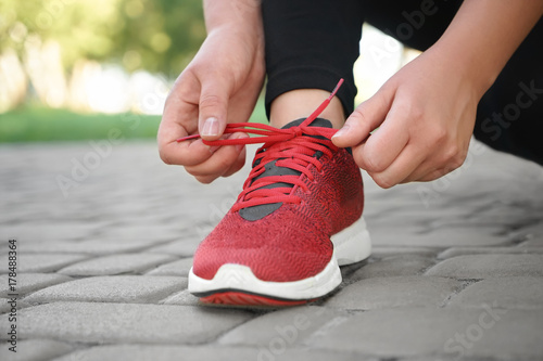 Young woman tying her shoelaces in park, closeup. Weight loss concept