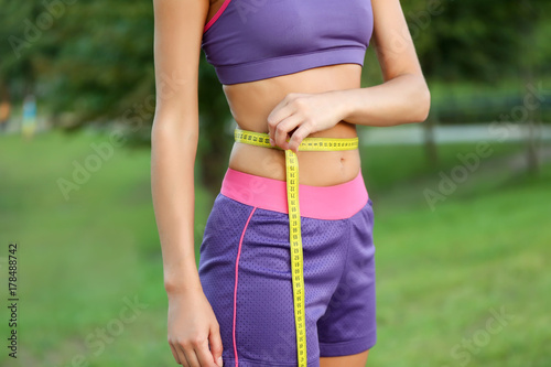 Beautiful young woman measuring her waist outdoors