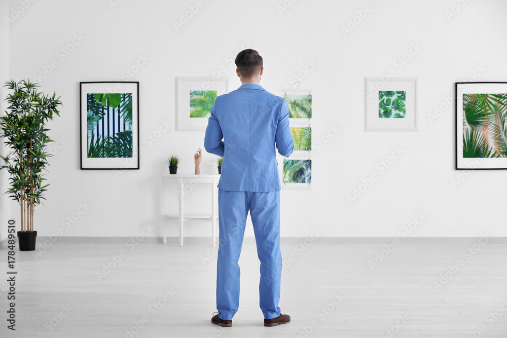 Young man looking at picture of tropical foliage in art gallery