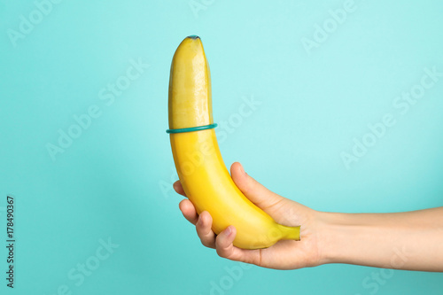 Woman holding banana with condom on color background photo