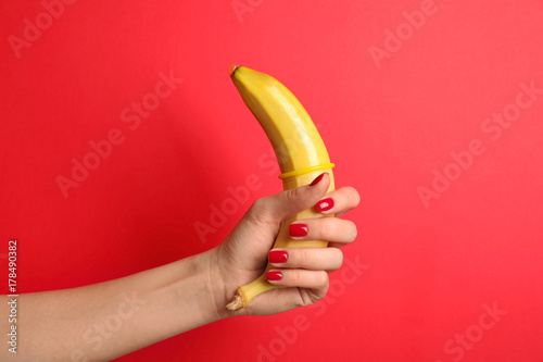 Woman holding banana with condom on red background