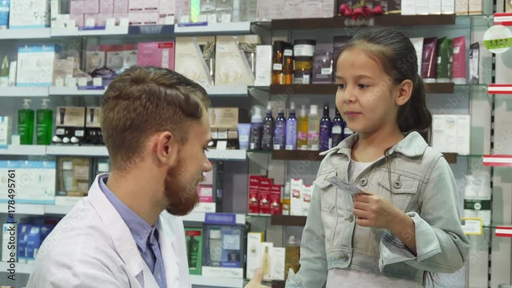 The chemist is sitting next to a little girl. She is unwell and he gives her the necessary pills. She smiles and shakes his hand. Mom and daughter are in the pharmacy The chemist is sitting next to a little girl. She is unwell and he gives her the necessary pills. She smiles and shakes his hand. Mom and daughter are in the pharmacy