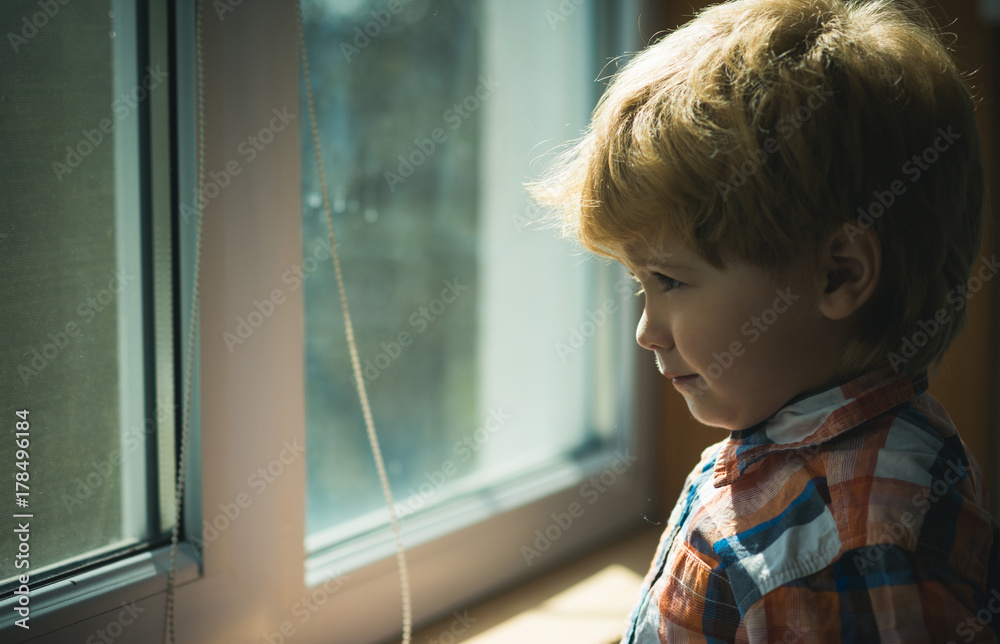 Child waiting parents and looks impatiently in the window. Sad cute boy near the window on a rainy day, waiting and hope Child waiting parents and looks impatiently in the window. Sad cute boy near the window on a rainy day, waiting and hope