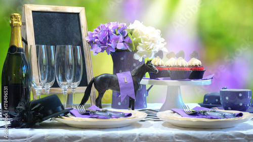 Horse racing Racing Day Luncheon fine dining table setting with small black fascinator hat, decorations and champagne, with light beam.