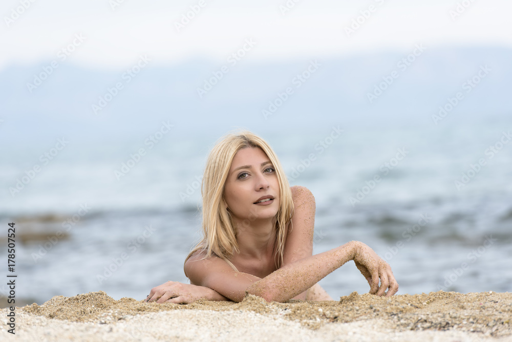 Slim gorgeous blonde woman lying topless on sand, photo in horizontal