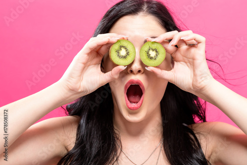  Happy young woman holding kiwis on a pink background