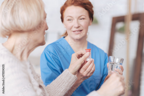 Cheerful nurse giving bottle with pill and water to patient