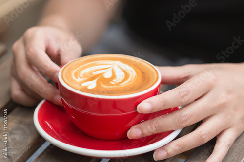 Woman hand holding a cup of latte coffee with latte art in the cafe.